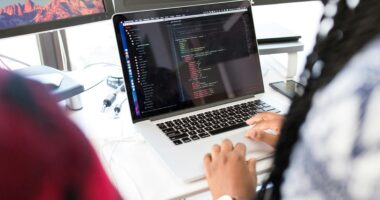 Pessoa programando em um laptop com código na tela.