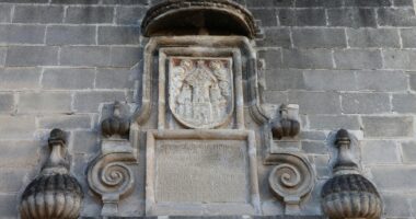 Escudo e inscrição em pedra na parede de um edifício histórico.